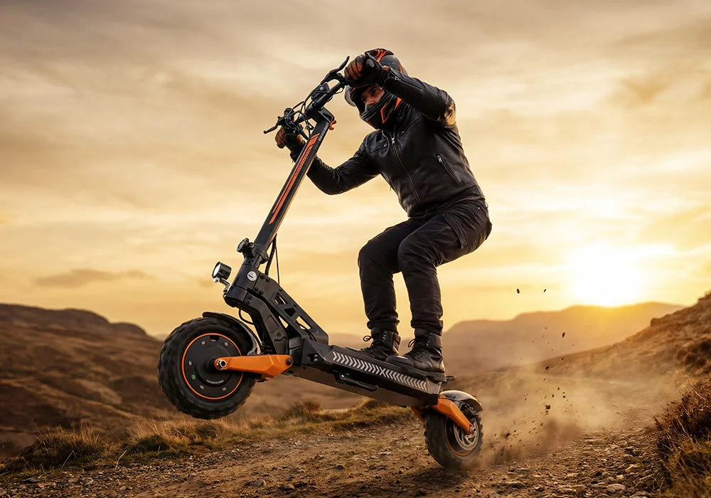 Un homme en tenue de protection effectuant une roue arrière sur une puissante trottinette électrique tout-terrain sur un sentier de montagne au coucher du soleil.